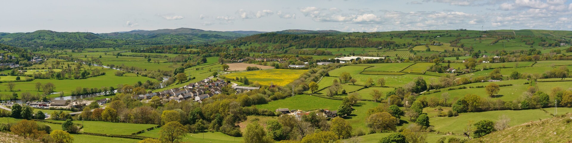 Rolling green hills, a village with houses, and a river.
