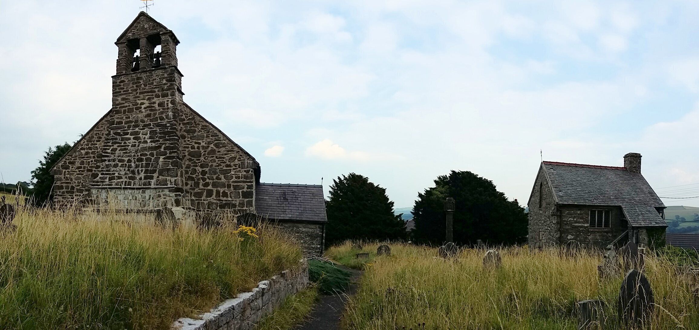 A stone church with a bell tower, surrounded by grass and a small path.