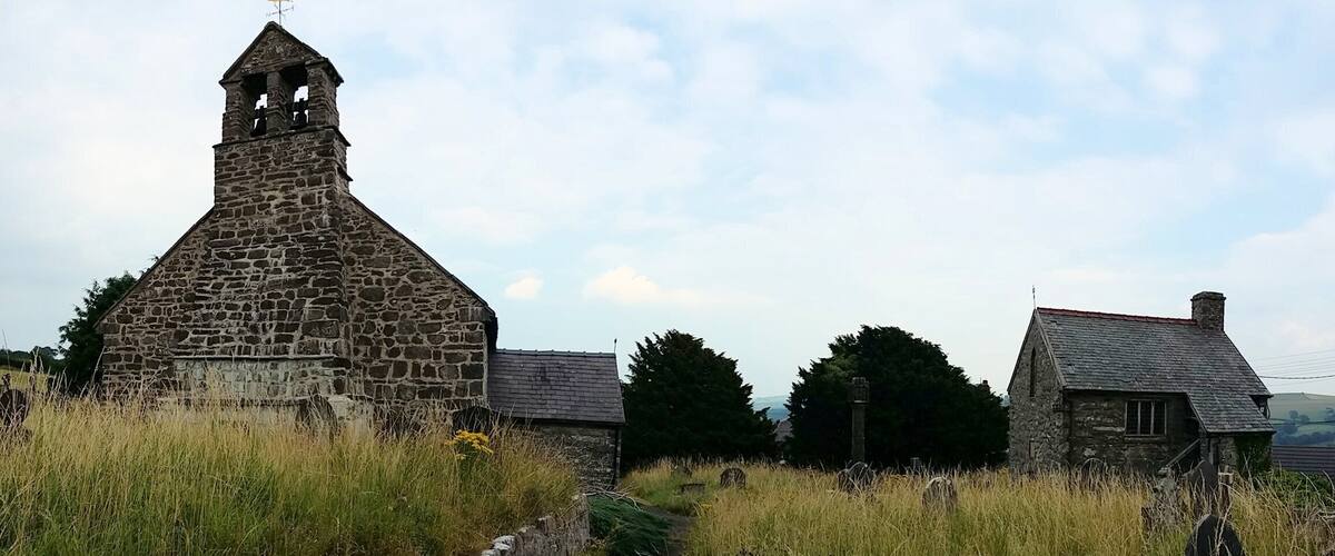 A stone church with a bell tower, surrounded by grass and a small path.