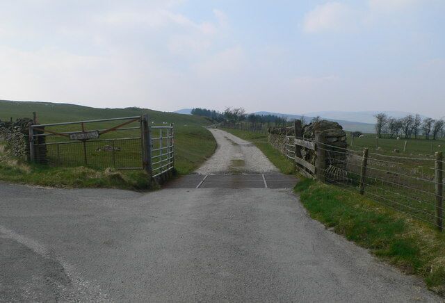 Un camino rural que lleva a una puerta con un muro de piedra y una valla de madera.