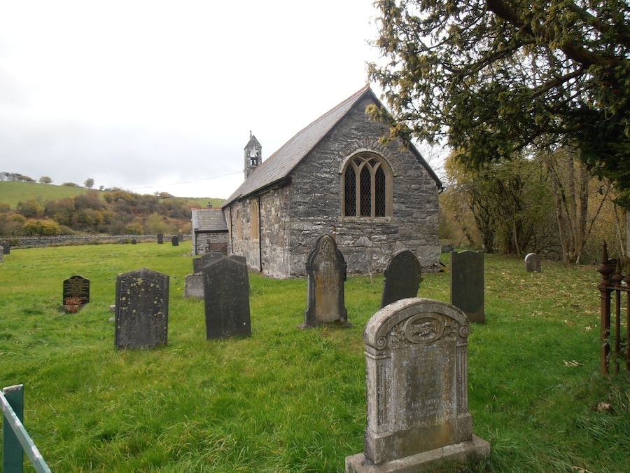 A stone church with a clock tower, surrounded by a cemetery with headstones.
