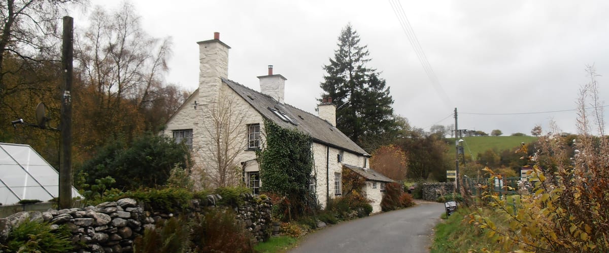 A narrow rural road flanked by stone walls and a stone house with ivy.
