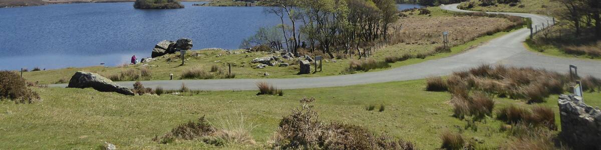 A lake surrounded by hills, a winding road, and a mountain in the background.