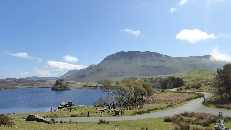 A lake surrounded by hills, a winding road, and a mountain in the background.