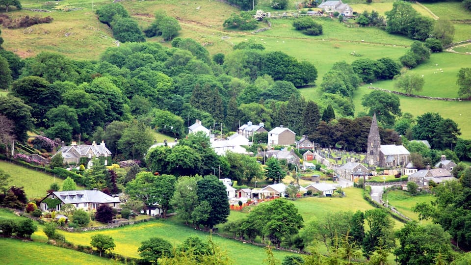A rural village with houses, a church, and rolling green hills.
