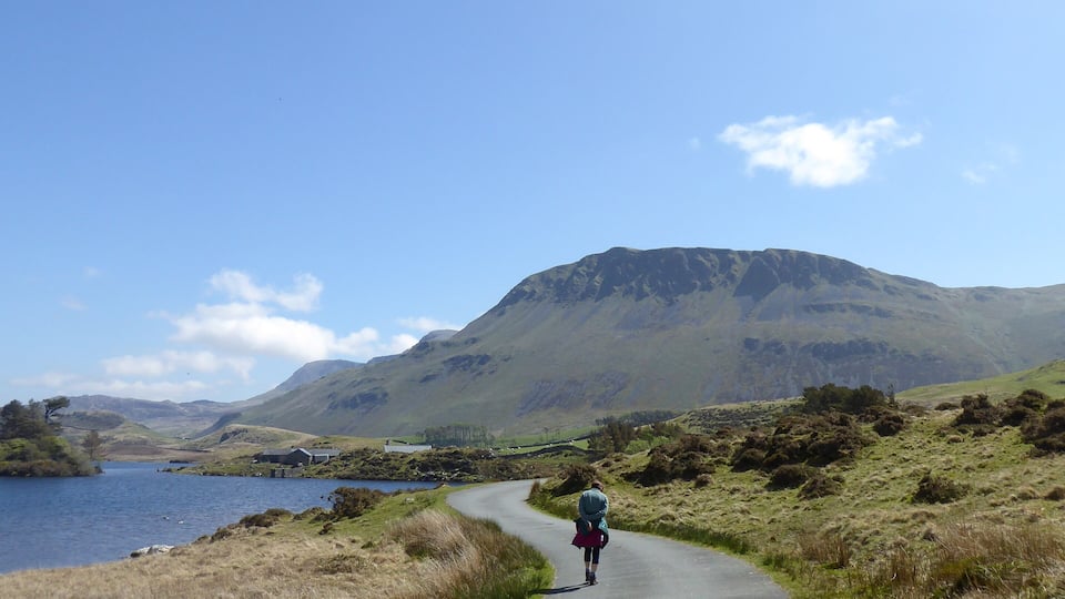 A winding road through a hilly landscape with a lake on one side and mountains in the background.