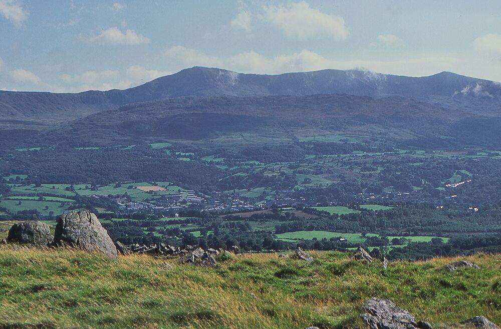 A mountainous landscape with a valley, scattered houses, and a prominent rock formation.