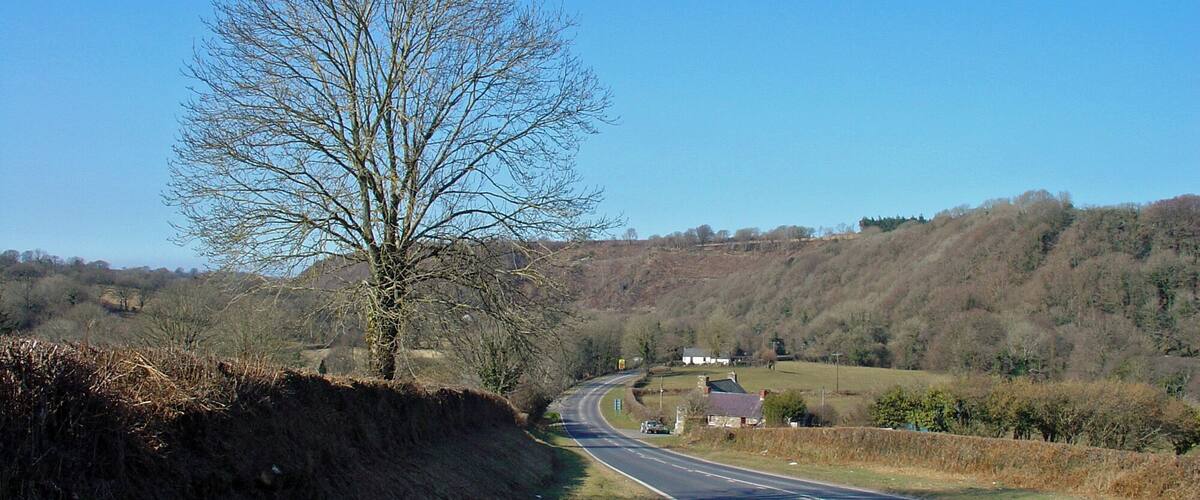 A rural road curving through a hilly landscape with sparse vegetation and a clear blue sky.