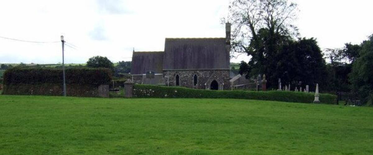 A grassy field with a stone building and a large barn in the background.