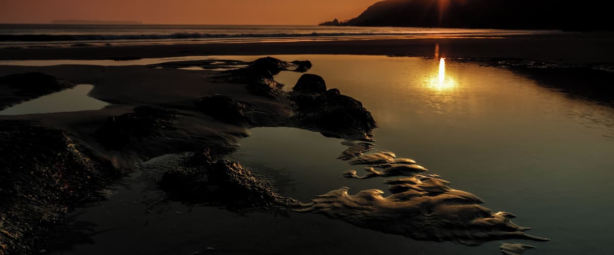 A sunset over a rocky beach with calm water reflecting the sky.