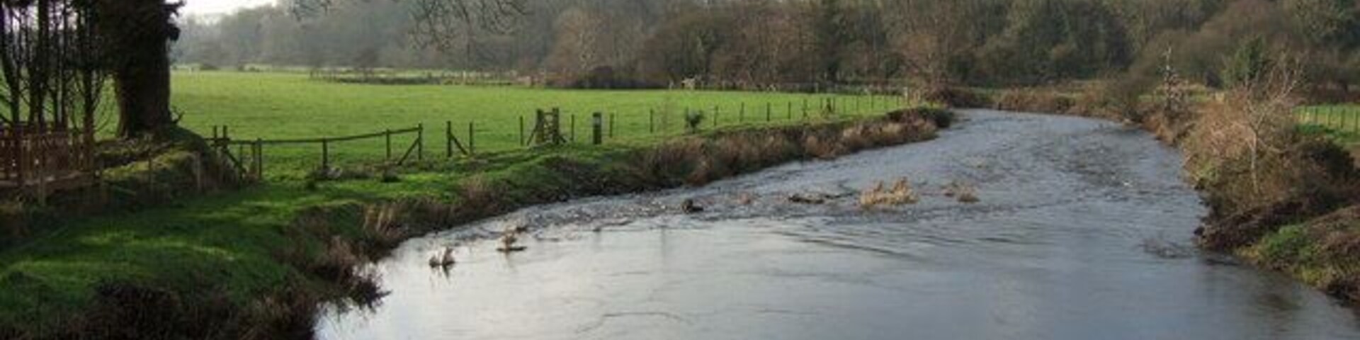 A river flowing through a rural landscape with a fence and trees.