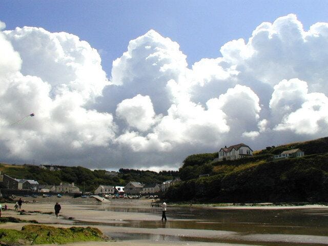 A coastal beach with houses and a large cloud-filled sky.