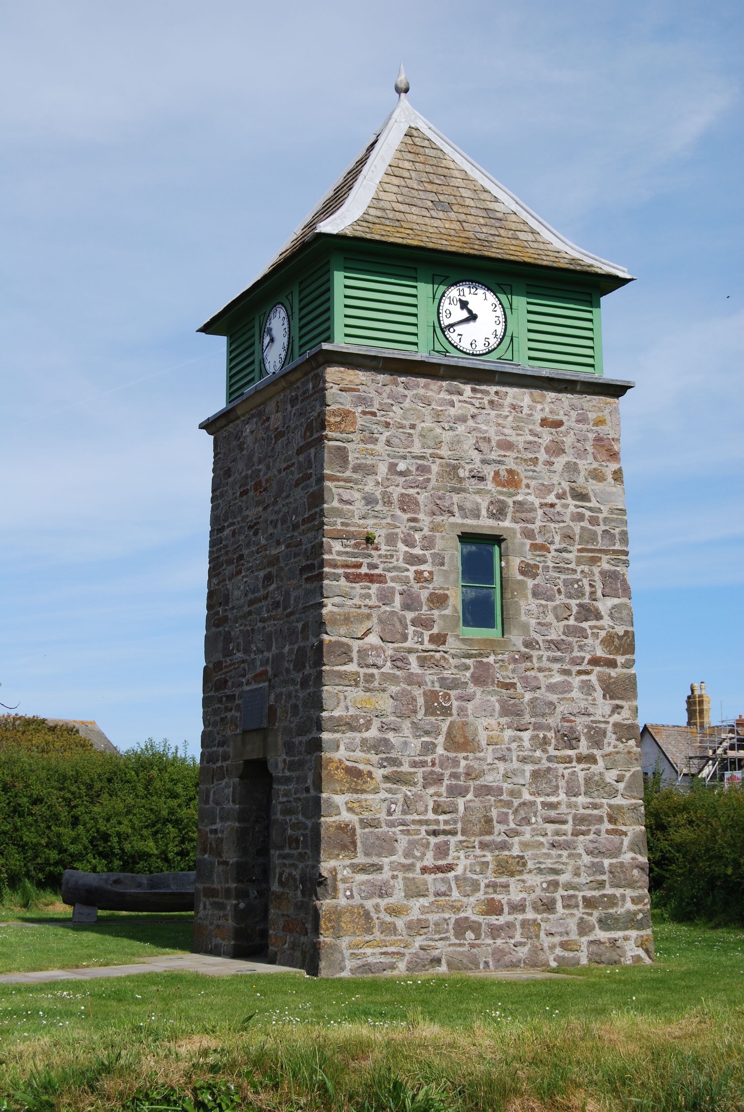 A stone clock tower with a green roof and two clocks.