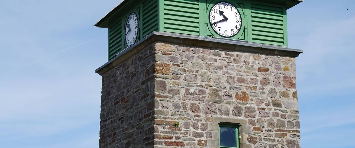 A stone clock tower with a green roof and two clocks.