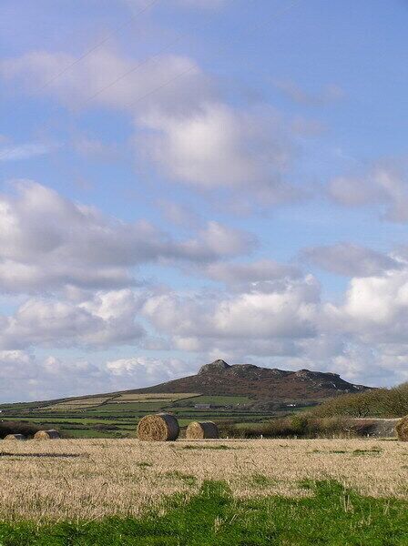 A rural landscape with rolling hills, hay bales, and a clear sky.