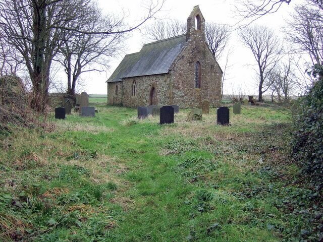 A stone church with a steep roof and a bell tower, surrounded by a grassy field and several headstones.