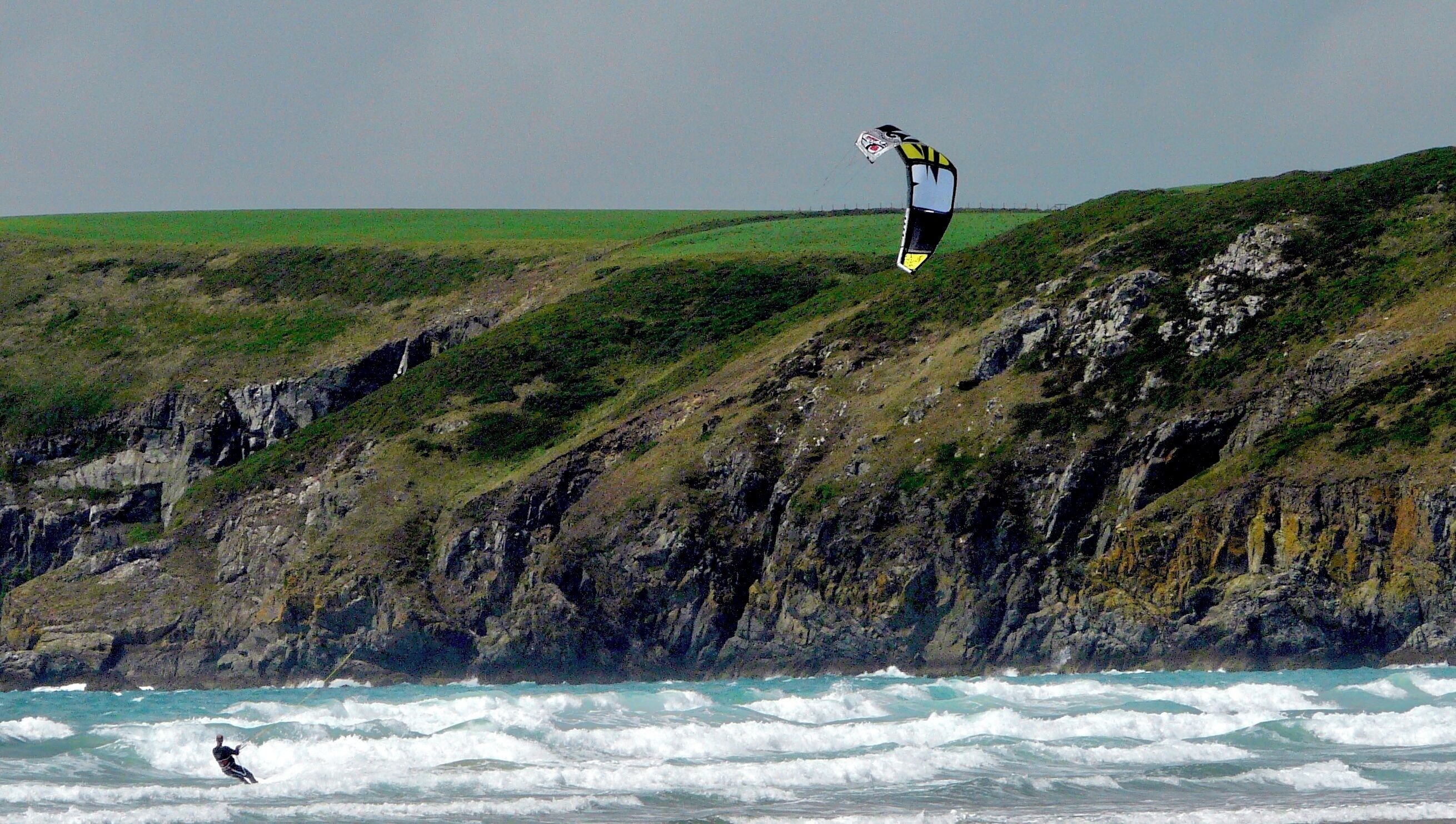 A person kite surfing on a cliff overlooking the ocean.