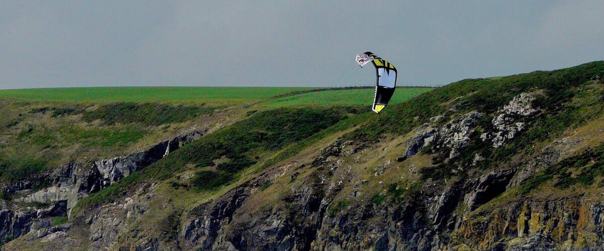 A person kite surfing on a cliff overlooking the ocean.