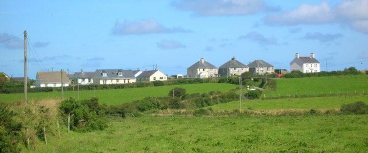 A rural landscape with green fields, several white houses, and a clear blue sky.