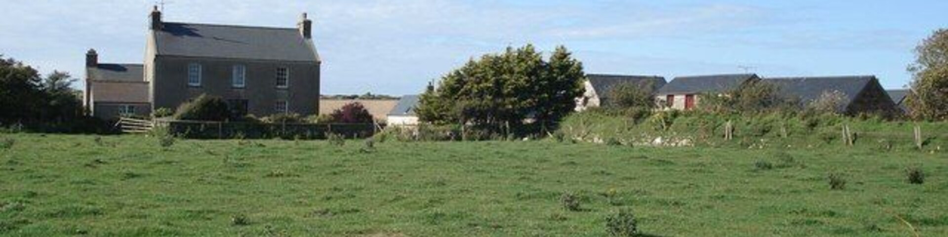 Paisagem rural com um amplo campo verde, uma casa e um celeiro.