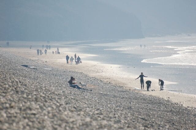 Una playa pedregosa con gente caminando y sentada.
