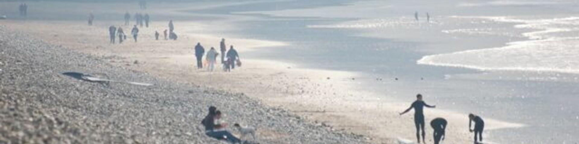 Una playa pedregosa con gente caminando y sentada.