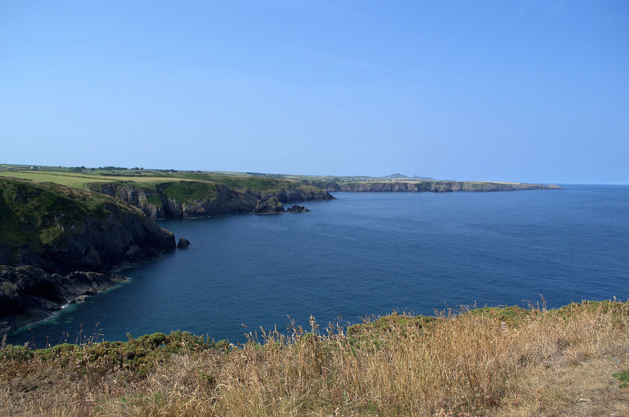 A coastal landscape with cliffs and a clear blue sea.