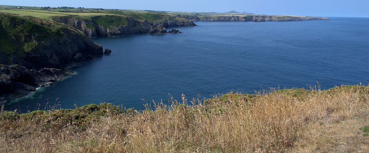 A coastal landscape with cliffs and a clear blue sea.
