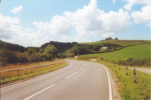 A curving road in a rural landscape with green fields and hills.