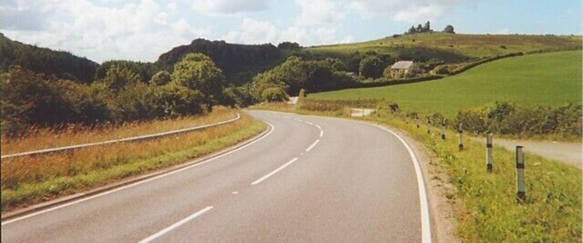 A curving road in a rural landscape with green fields and hills.