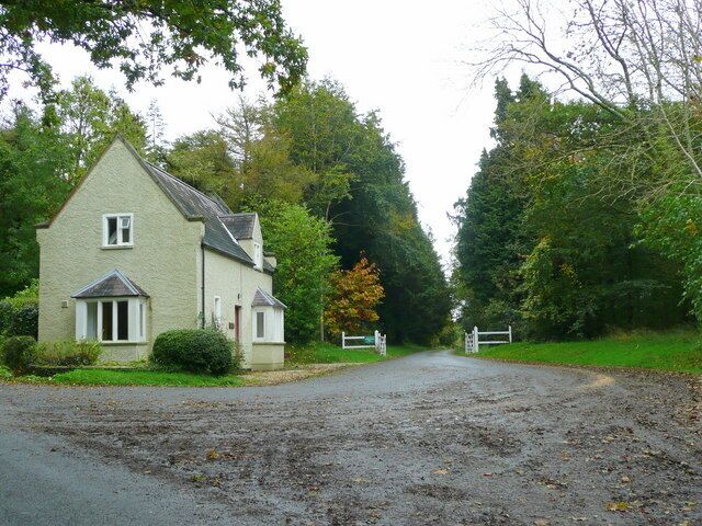 A rural road leading to a house with a gated entrance, surrounded by trees and greenery.