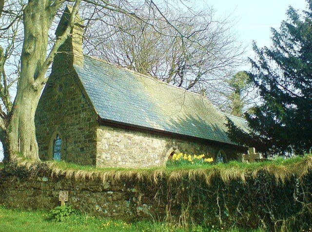 A stone church with a steeply pitched roof and a stone wall in front.
