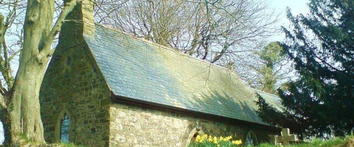A stone church with a steeply pitched roof and a stone wall in front.