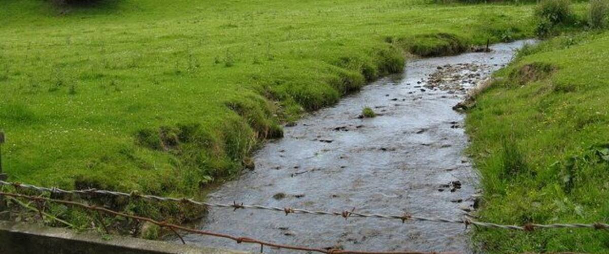 A rural landscape with a stream, green fields, and rolling hills.