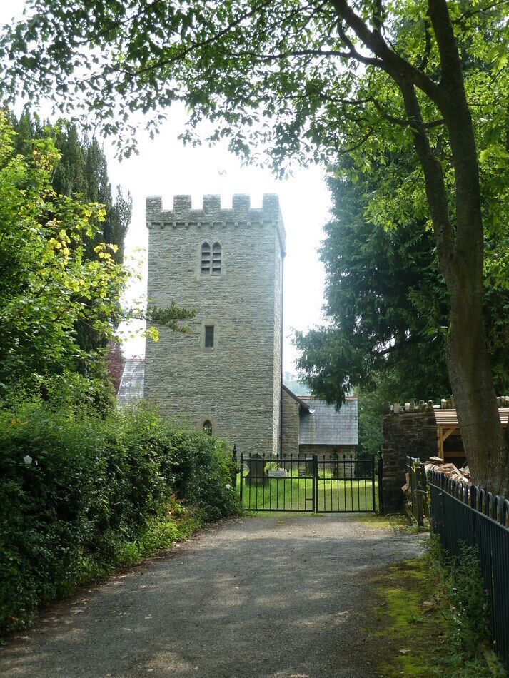 A stone tower surrounded by lush greenery and a gravel path leading to a black metal gate.