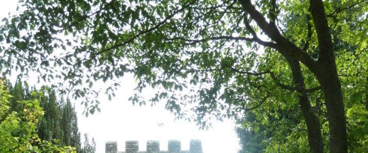 A stone tower surrounded by lush greenery and a gravel path leading to a black metal gate.