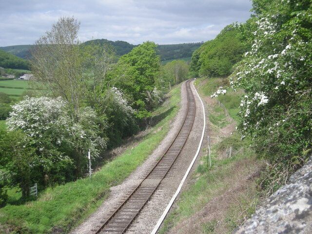 A railway track curving through a green landscape with trees and a fence.