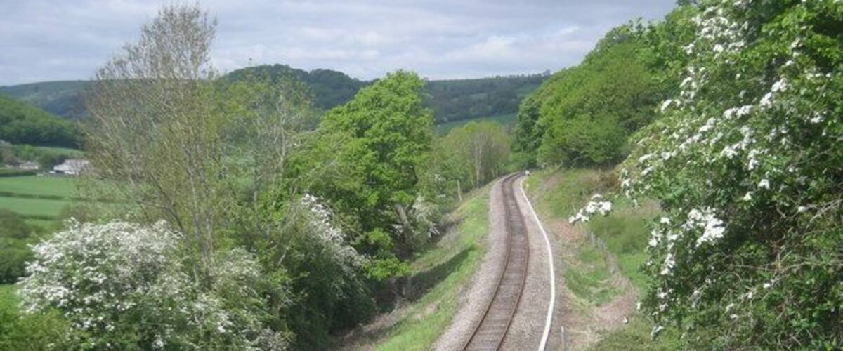 A railway track curving through a green landscape with trees and a fence.