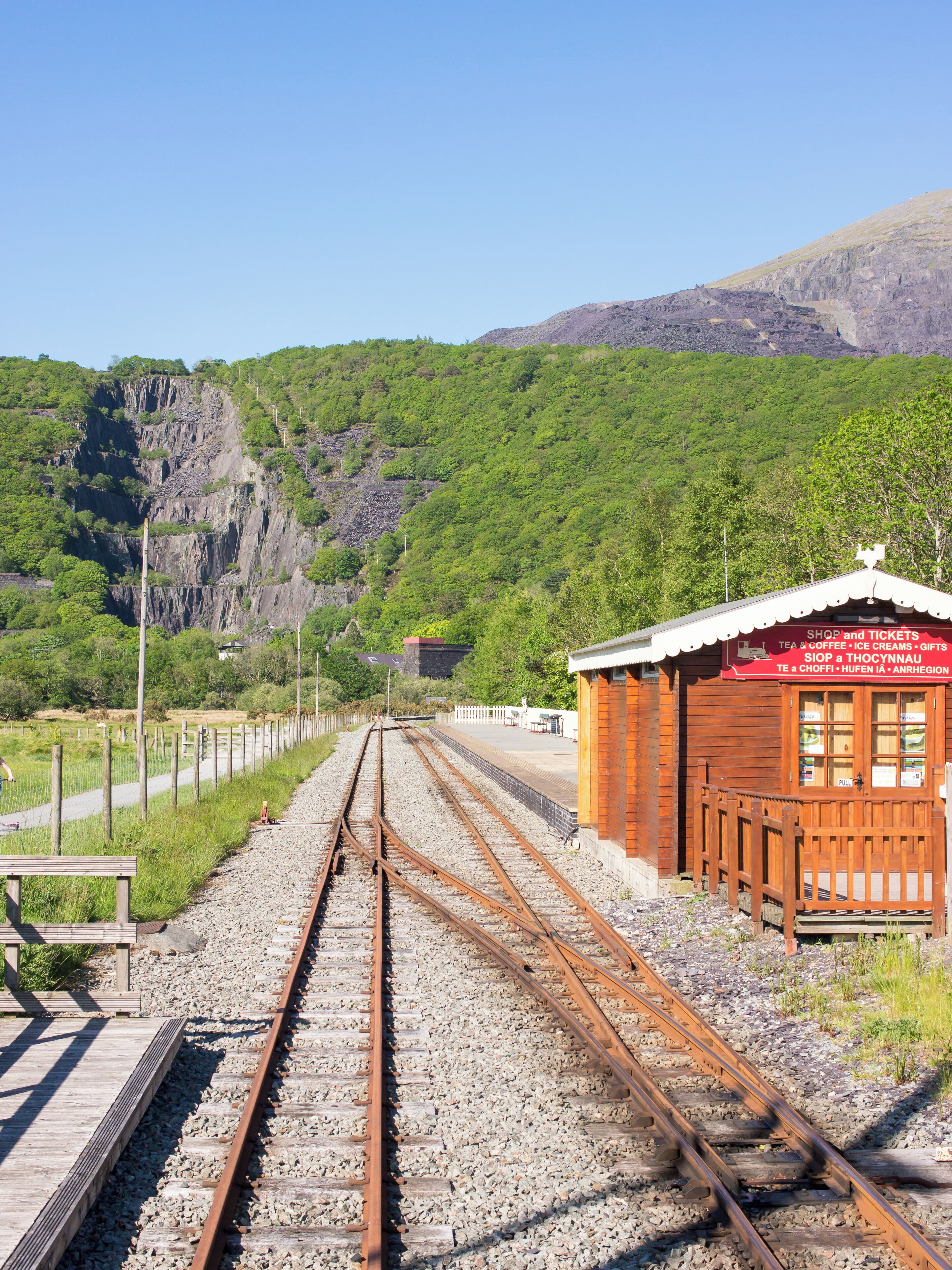 A railway track leading to a small wooden building with a signboard.