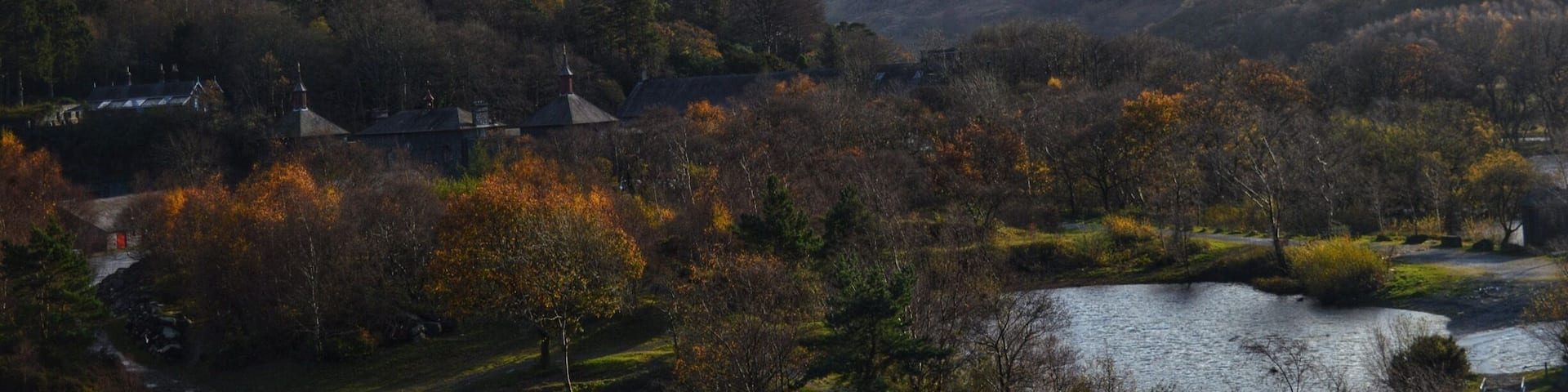 A mountainous landscape with a lake, autumn-colored trees, and a few buildings.