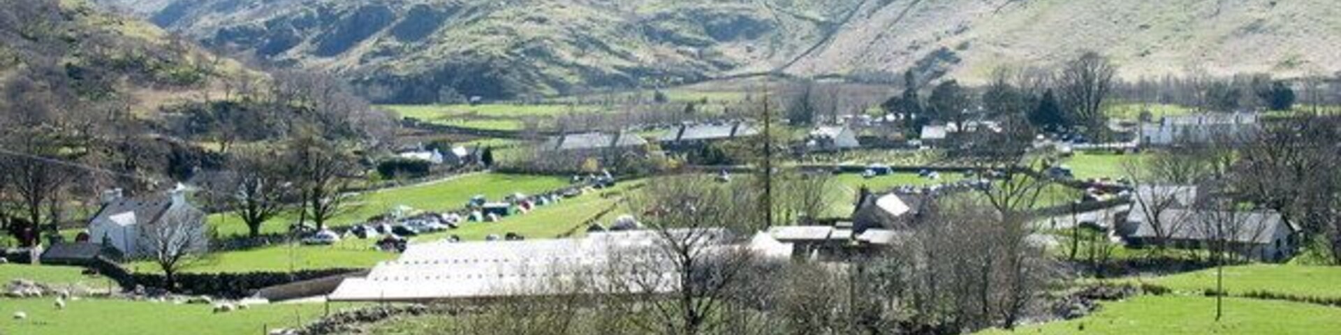 Un paisaje rural con colinas ondulantes, casas dispersas y un pequeño arroyo.