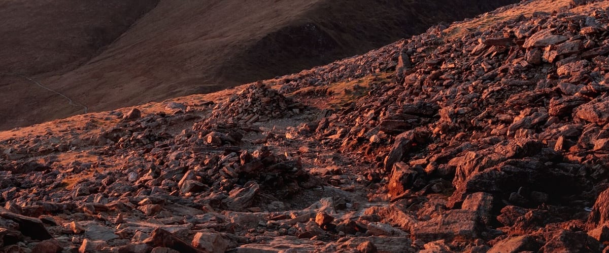 A mountainous landscape with rocky terrain and a sunset in the background.