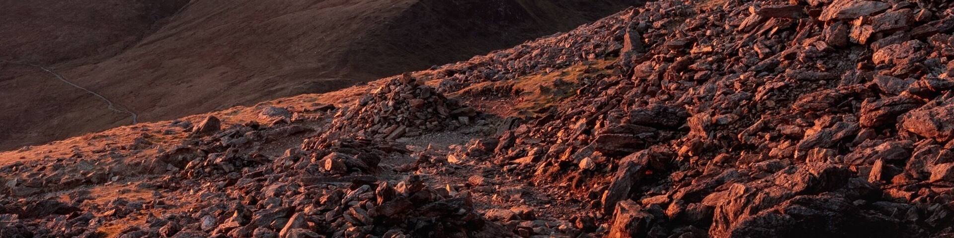 A mountainous landscape with rocky terrain and a sunset in the background.