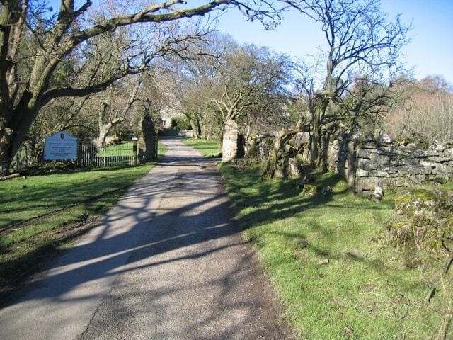 A paved path flanked by trees and stone walls, leading to a stone archway.