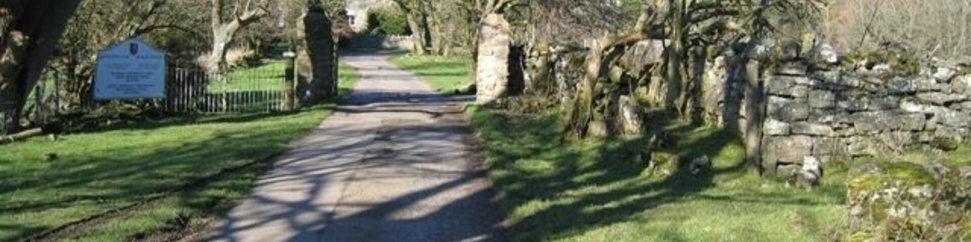 A paved path flanked by trees and stone walls, leading to a stone archway.
