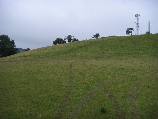 Uma colina gramada com uma cerca e uma torre de telefonia ao longe.
