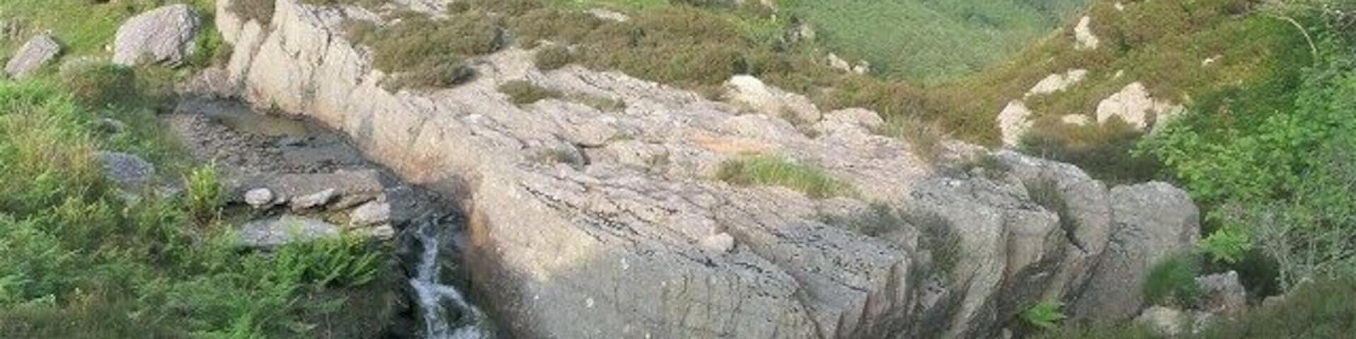 Giant slab above Nant Rhaeadr falls This huge slab obstructs the flow of the river to such a degree that it appears on the 1:25K map. The water flows around three sides of it before falling down to the valley below. A wall has been built beside the slab to narrow the flow. This can be seen where the white water appears in the photo.