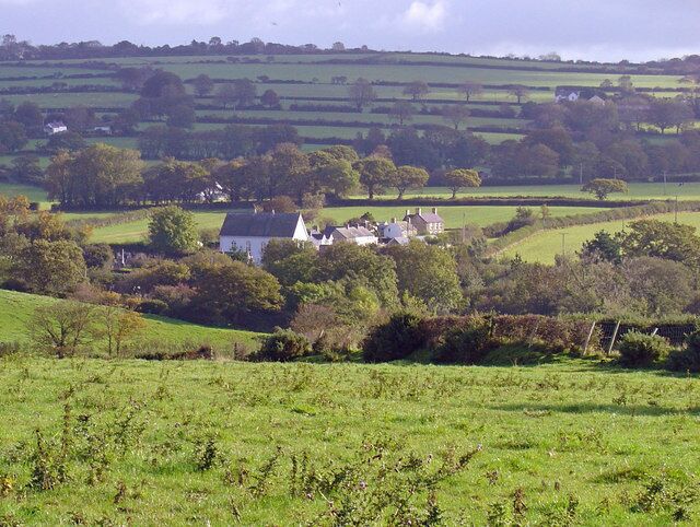 Rolling green hills, a white house with a pointed roof, and scattered trees.