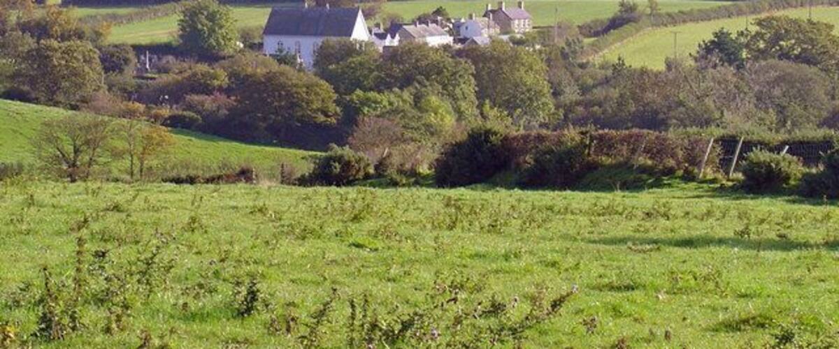 Rolling green hills, a white house with a pointed roof, and scattered trees.