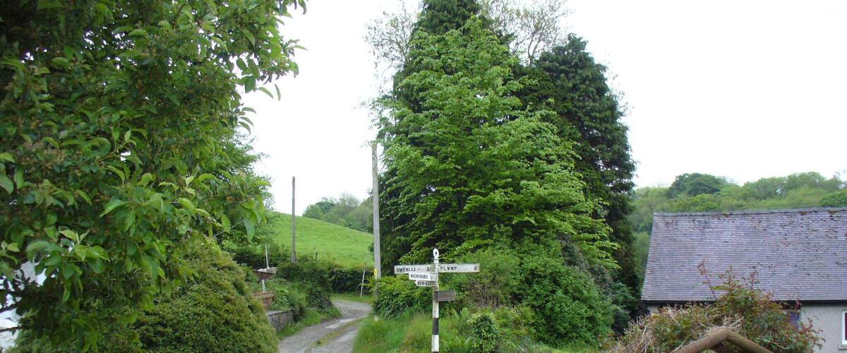A rural road with a directional signpost, lush greenery, and a stone wall.